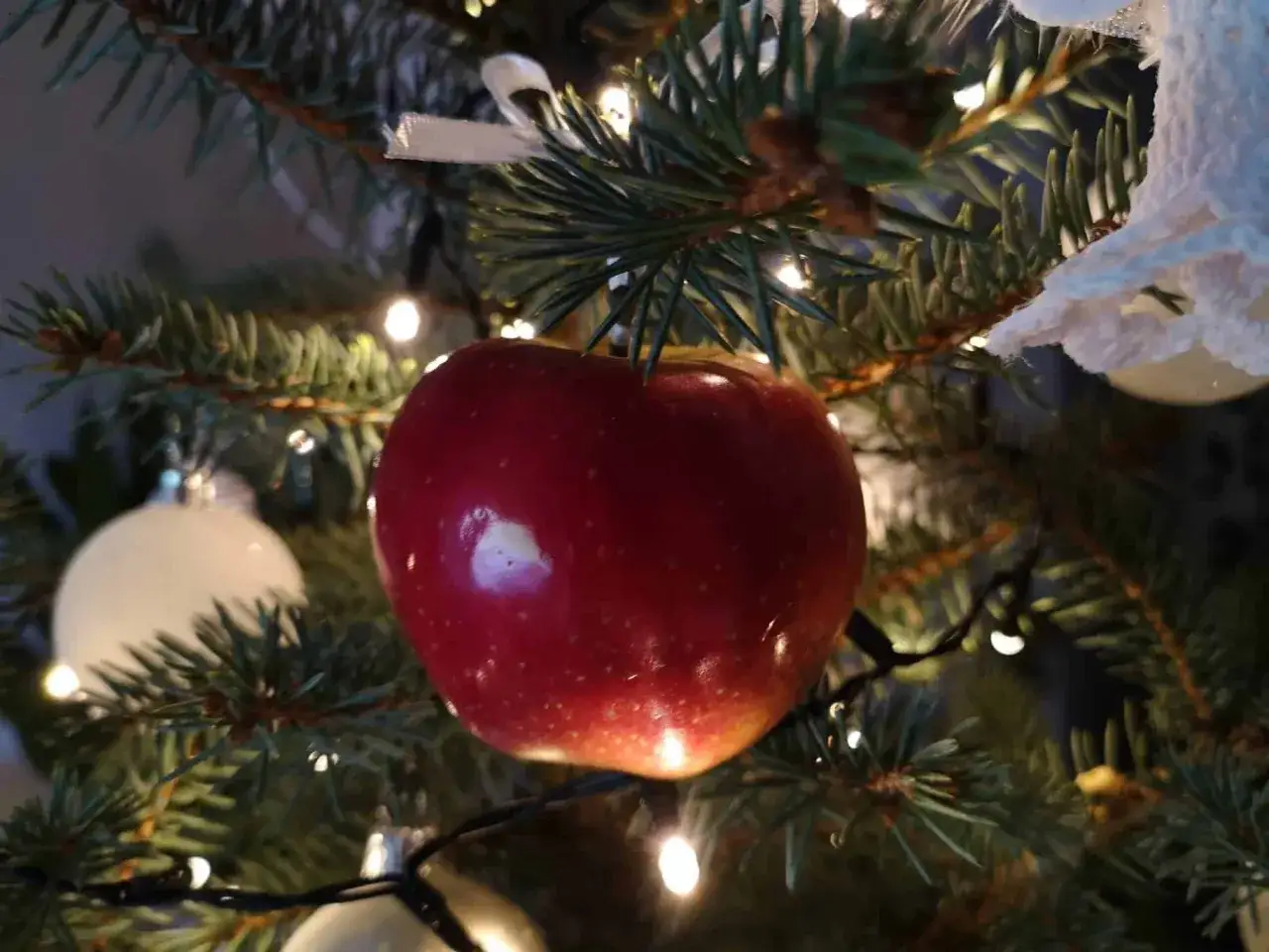 Czerwone jabłko, symbol świąt, wisi na choince wśr&oacute;d lampek i bombek.