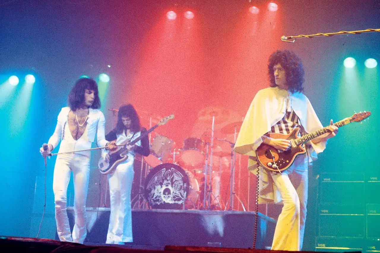 Freddie Mercury i Brian May na scenie, w tle perkusja. Ich stroje i gra sugerują emocjonalną interpretację 