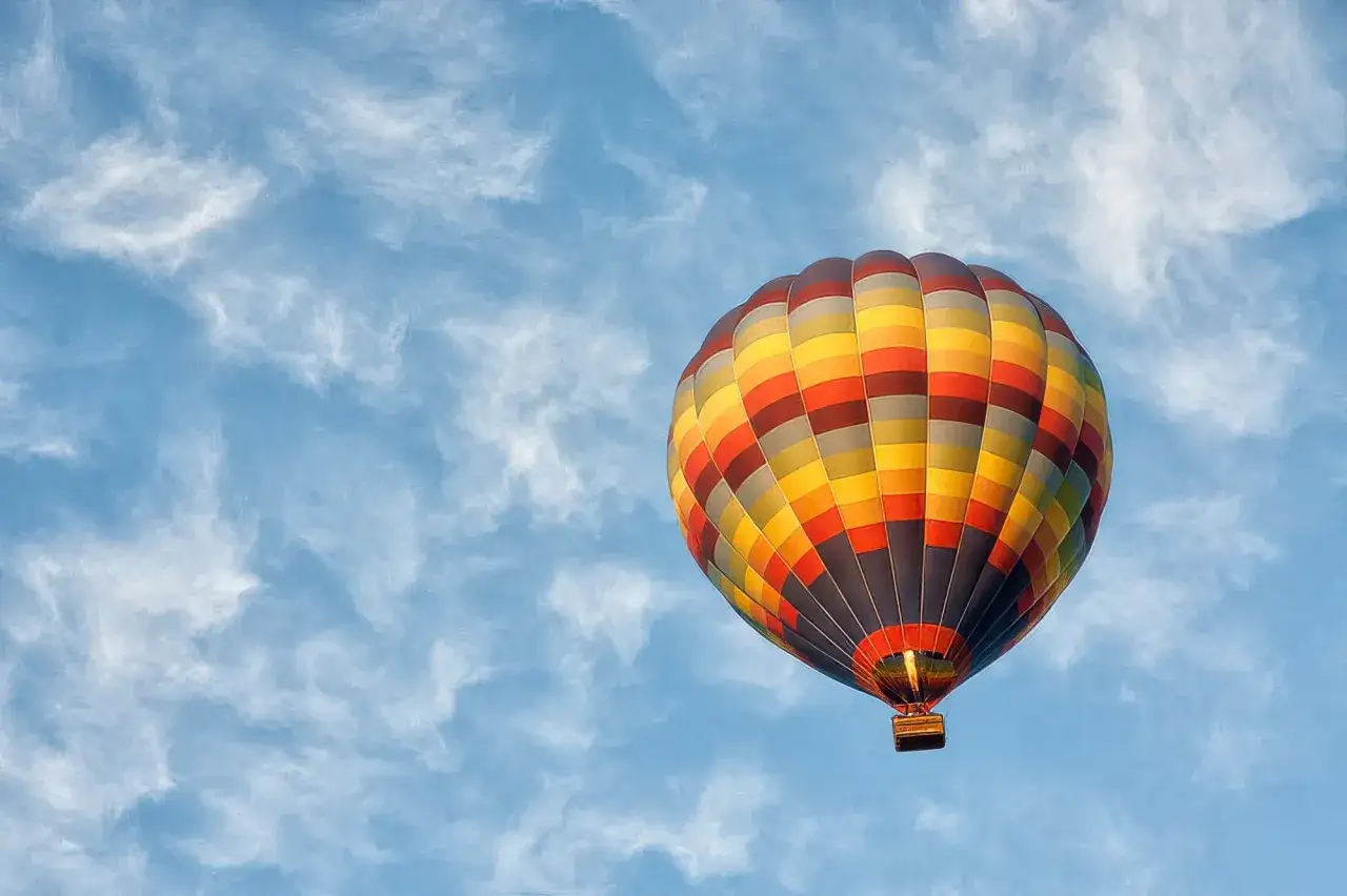 Kolorowy balon na ogrzane powietrze na tle błękitnego nieba z chmurami. Idealny prezent, co można kupić na 50 urodziny – niezapomniane wrażenia!