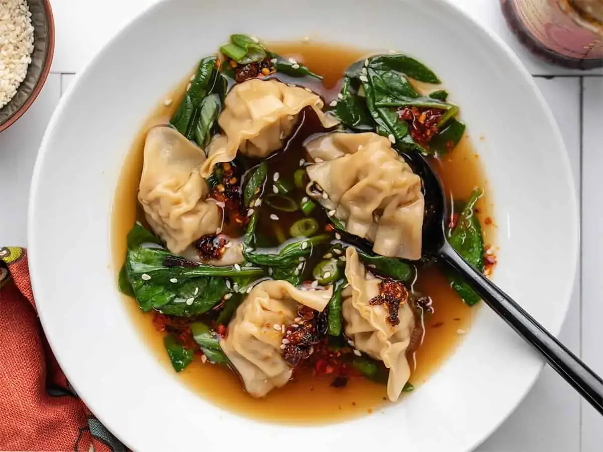 Aromatyczna zupa wonton z zielonymi warzywami i sezamem, podana w białej misce.