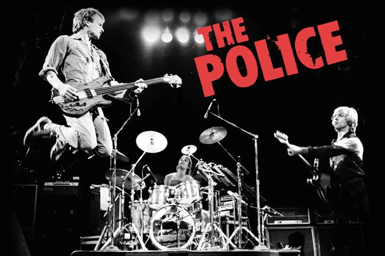 Wokalista The Police, Sting, skacze na scenie z gitarą basową. Obok perkusista i gitarzysta.