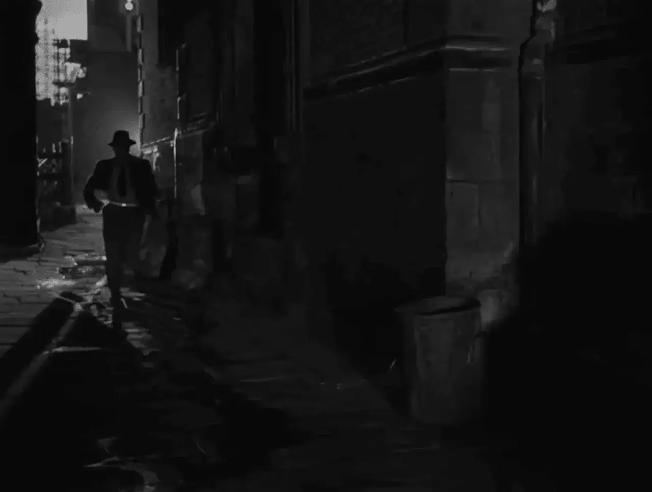 Un uomo con cappello cammina in un vicolo buio, tipico di un **genere noir film**. Ombre lunghe e un'atmosfera tesa.