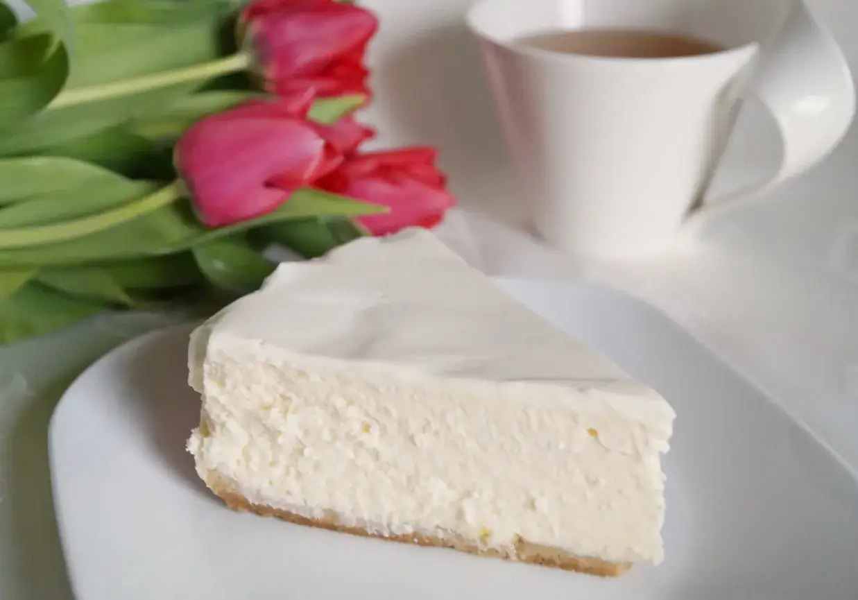 Pyszny sernik z mascarpone, idealny na każdą okazję. Obok filiżanka herbaty i bukiet różowych tulipanów.