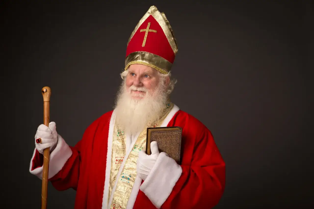 Ein Mann im Bischofsornat mit Mitra und Stab, der ein Buch h&auml;lt. Er erinnert an die Legende von Nikolaus von Myra, der f&uuml;r seine Gro&szlig;z&uuml;gigkeit bekannt war.