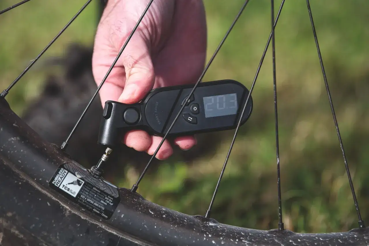 Comprobando la presión de las ruedas de bici con un medidor digital. La pantalla muestra 20.3 PSI.