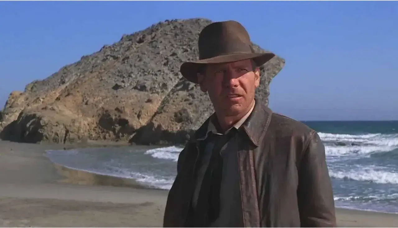 Indiana Jones, con su ic&oacute;nico sombrero y chaqueta de cuero, se encuentra en una playa rocosa de Almer&iacute;a, listo para una nueva aventura.