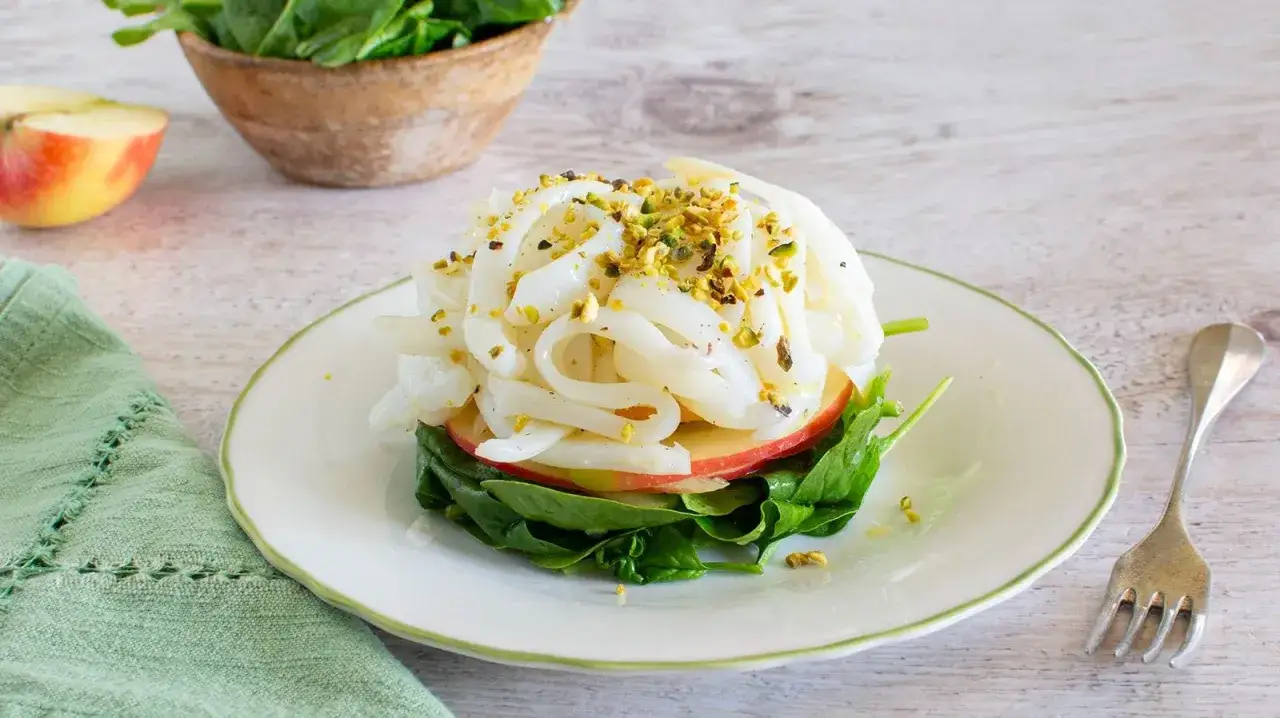 Delicata tagliatella di mare su letto di spinaci e fettine di mela, guarnita con pistacchi tritati.
