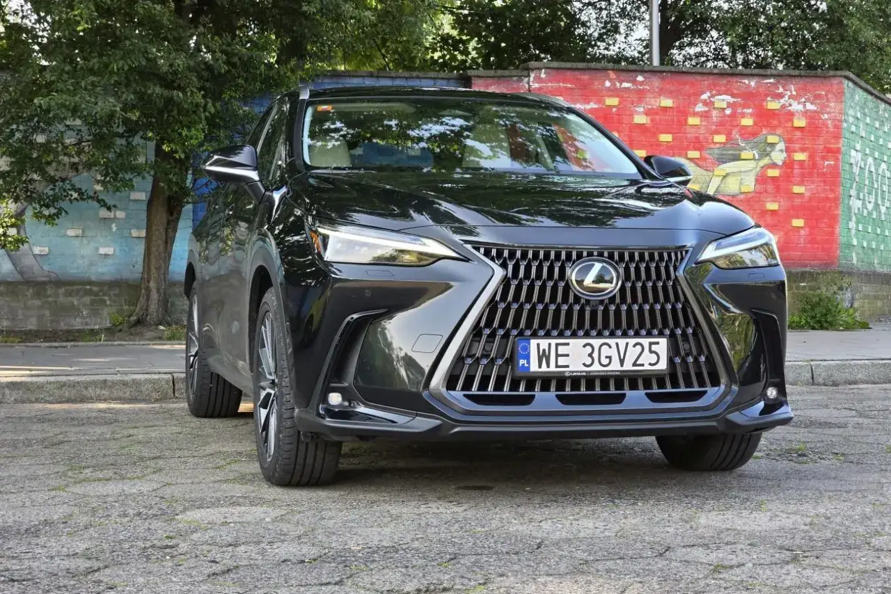 Elegancki, czarny Lexus 350h z charakterystycznym grillem i światłami LED, zaparkowany przed kolorową ścianą z muralem.