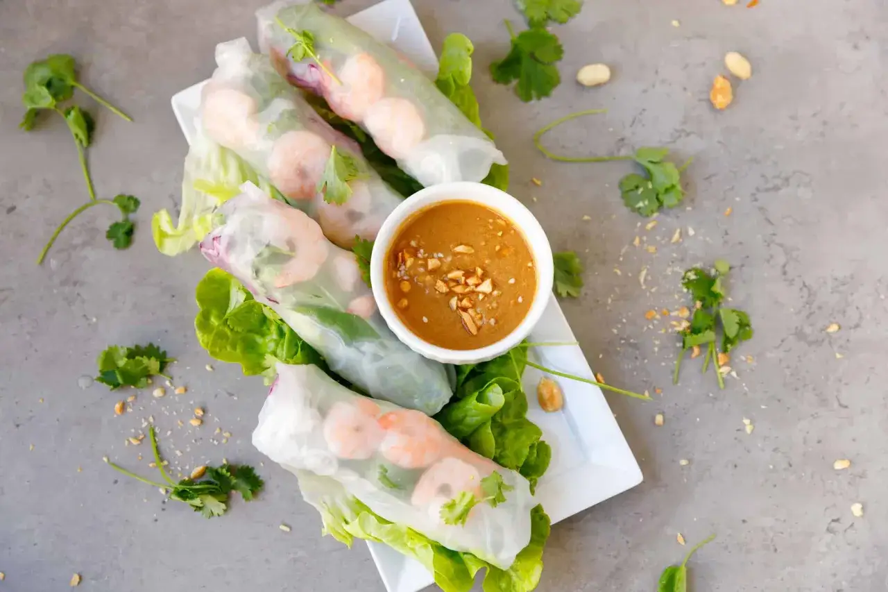 Świeże spring rolls z krewetkami, sałatą i kolendrą, podane z orzechowym sosem. Idealne na lekki posiłek.