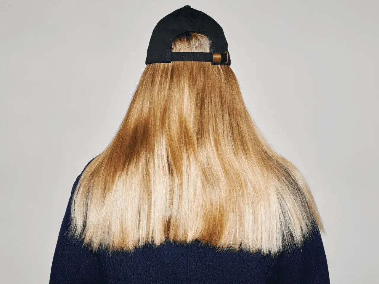En person med långt, blont hår och en svart keps. Håret har en naturlig glans, som om det vore lätt att ljusa upp håret utan blekning.