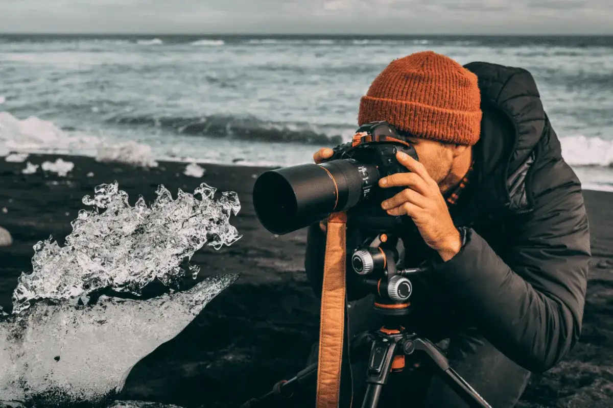 Photo macro d'un photographe capturant la beaut&eacute; glac&eacute;e d'un &eacute;clat de glace sur une plage de sable noir, avec l'oc&eacute;an en arri&egrave;re-plan.