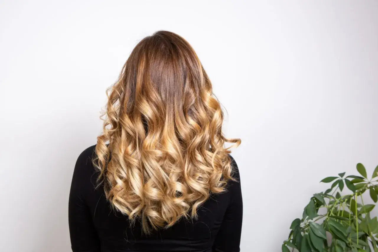 Chevelure ondulée avec un balayage chatain clair subtil, créant un effet ensoleillé naturel.