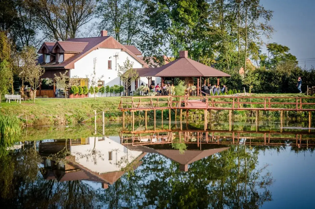 Malownicze agroturystyka w dolinie stawów. Dom z altaną i pomostem odbijają się w spokojnej tafli wody.