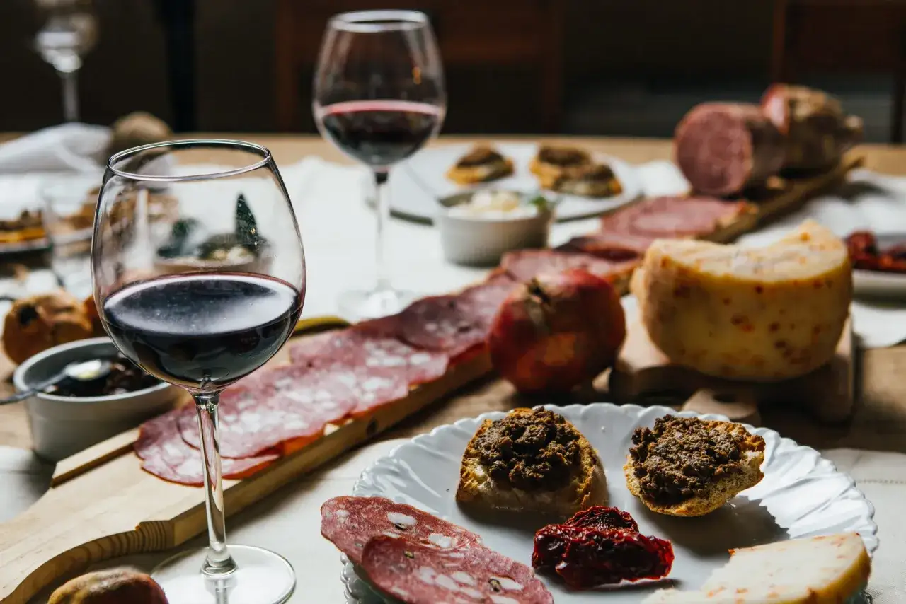 Un tavolo imbandito con salumi, formaggi, crostini e vino rosso, un assaggio delle cose tipiche toscane.