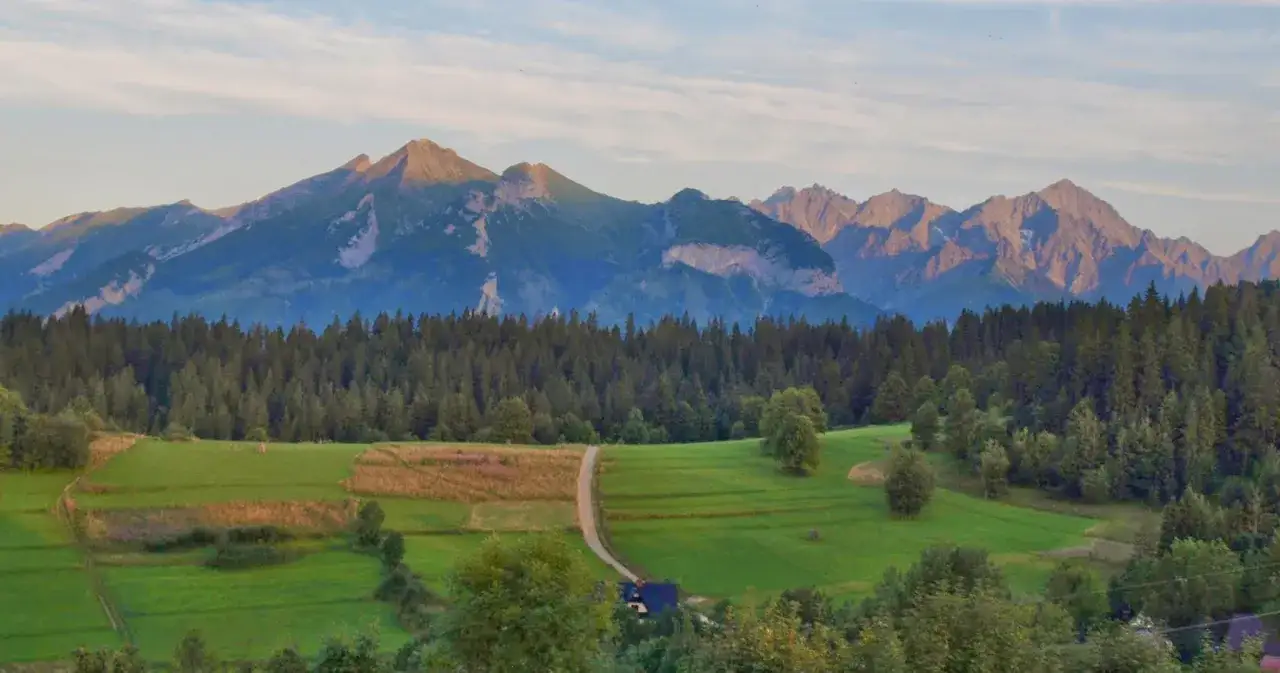 Majestatyczne Tatry Bielskie w blasku słońca, otoczone gęstym lasem i zielonymi polami.