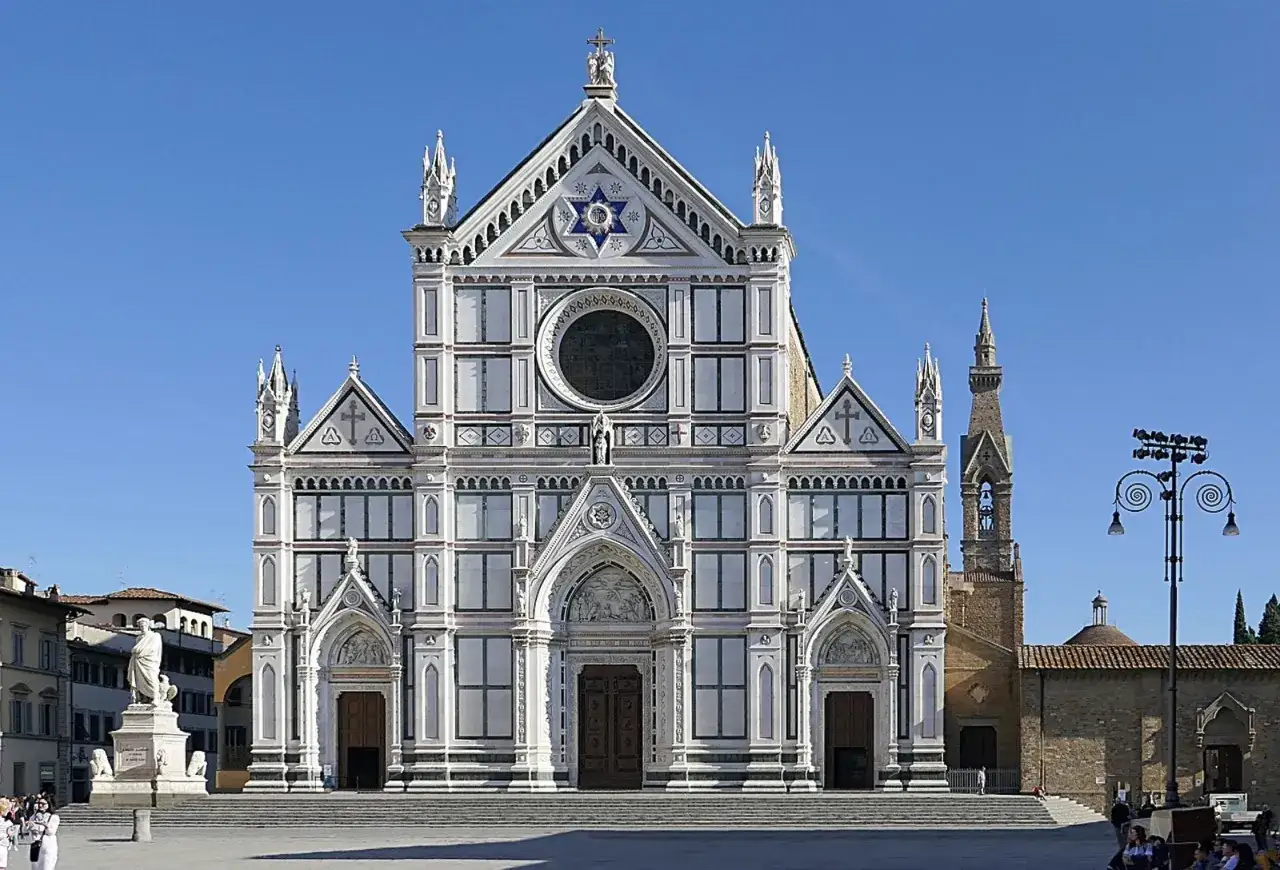 La Basilica di Santa Croce a Firenze, con la sua facciata bianca e verde, domina la piazza. Un cielo azzurro la sovrasta.
