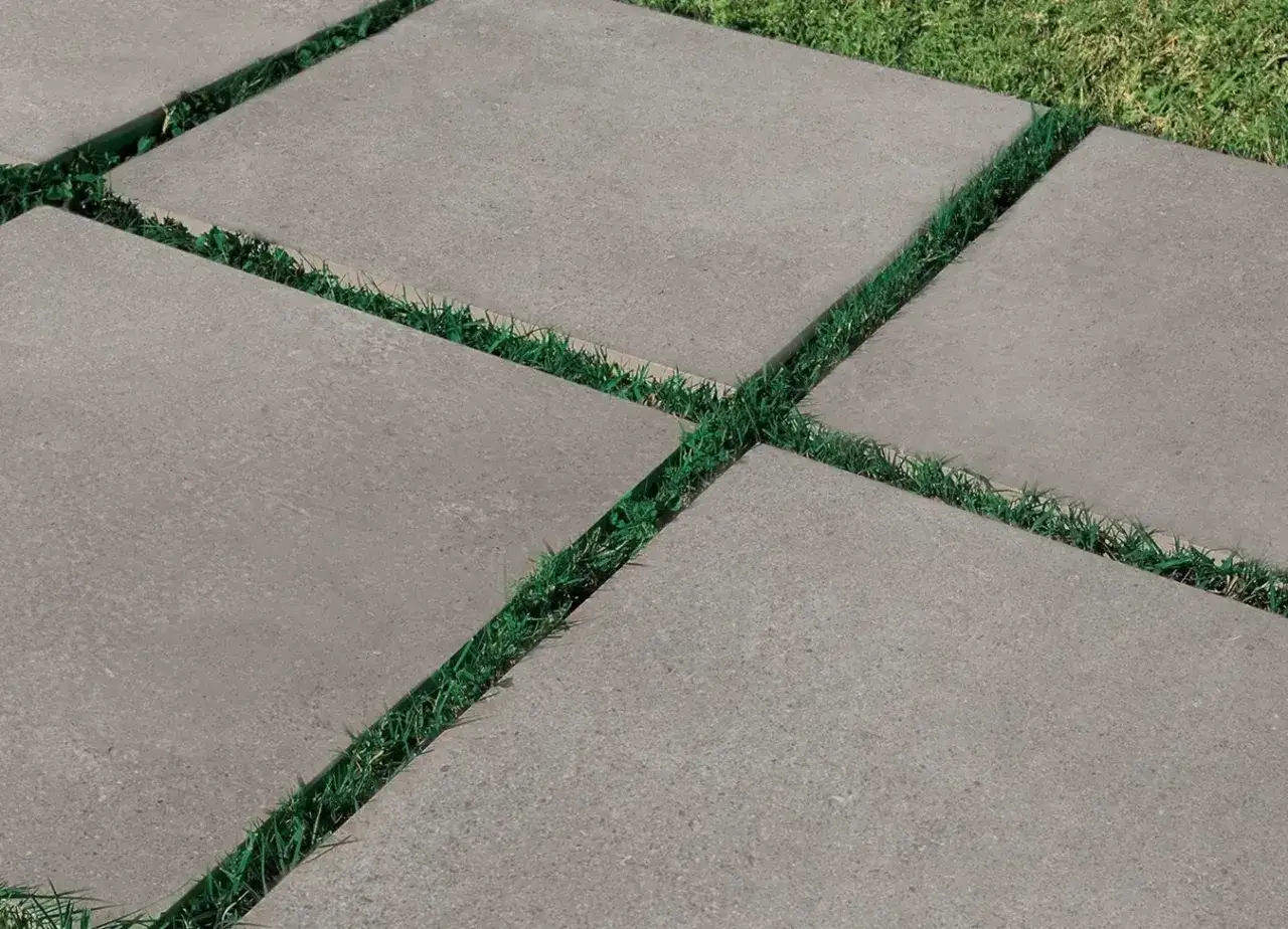 Posa a secco di pavimenti esterni con lastre quadrate grigie alternate a strisce di erba verde.