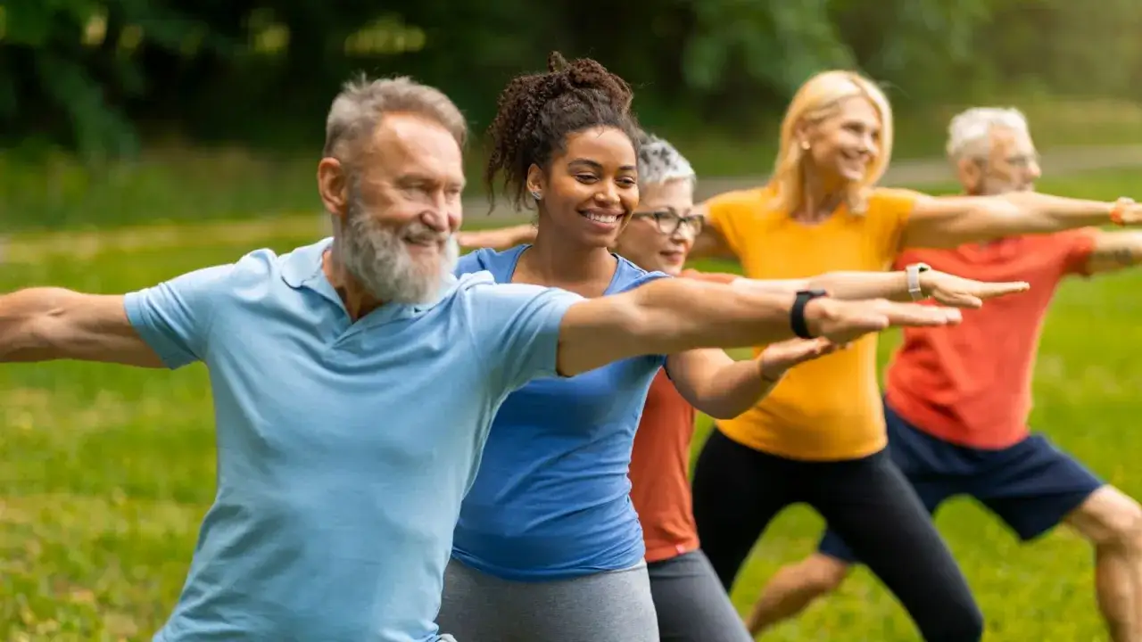 Gruppe von Menschen unterschiedlichen Alters &uuml;bt Yoga im Freien. Sie l&auml;cheln und bewegen sich synchron, um geistig fit zu bleiben.