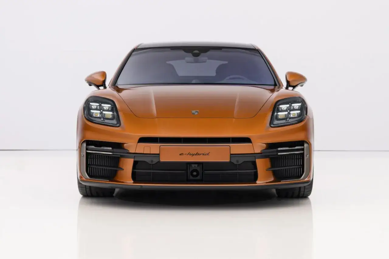 Pomarańczowy Porsche Panamera 2024 e-hybrid prezentuje się imponująco z przodu, z charakterystycznymi reflektorami i sportowym grillem.