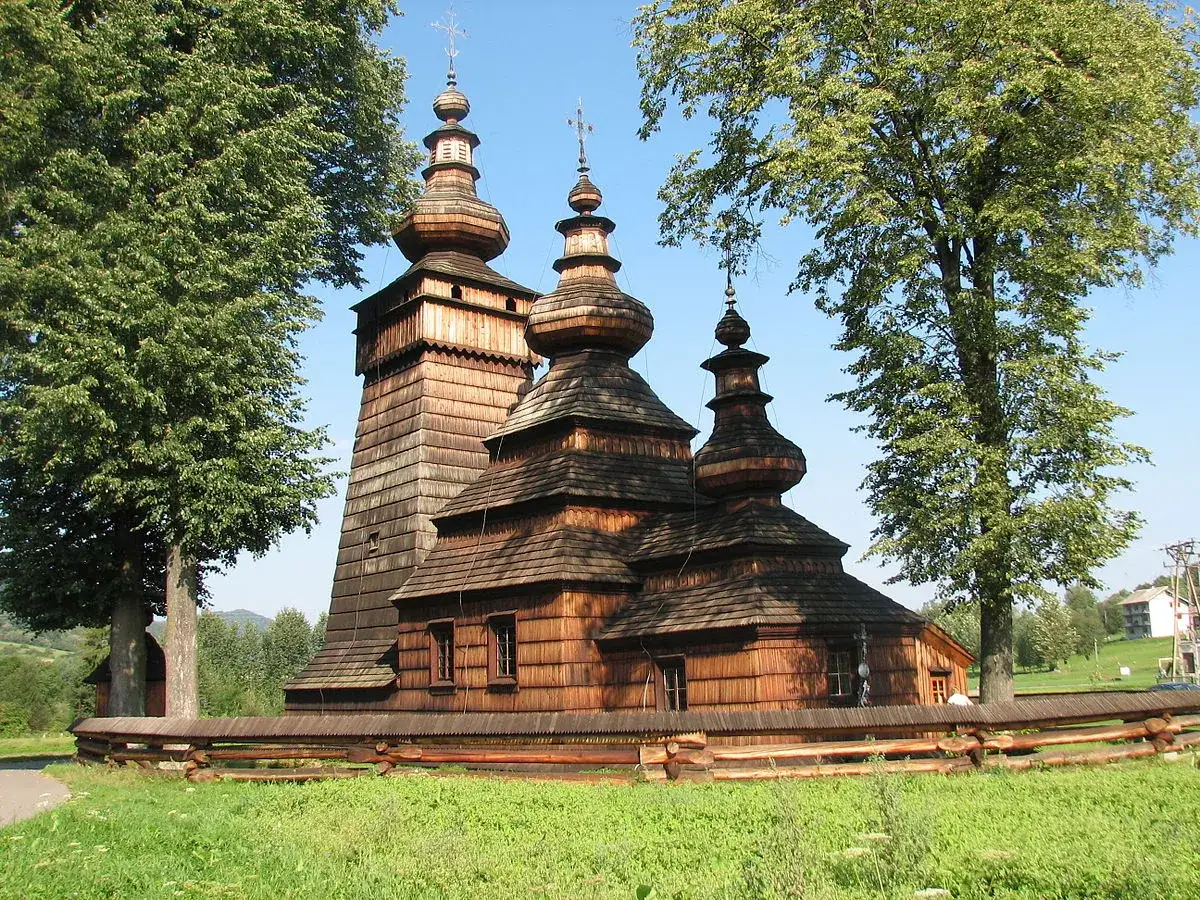 Drewniana cerkiew, jeden z pięknych zabytków w Polsce, z charakterystycznymi kopułami i wieżą, otoczona zielenią.