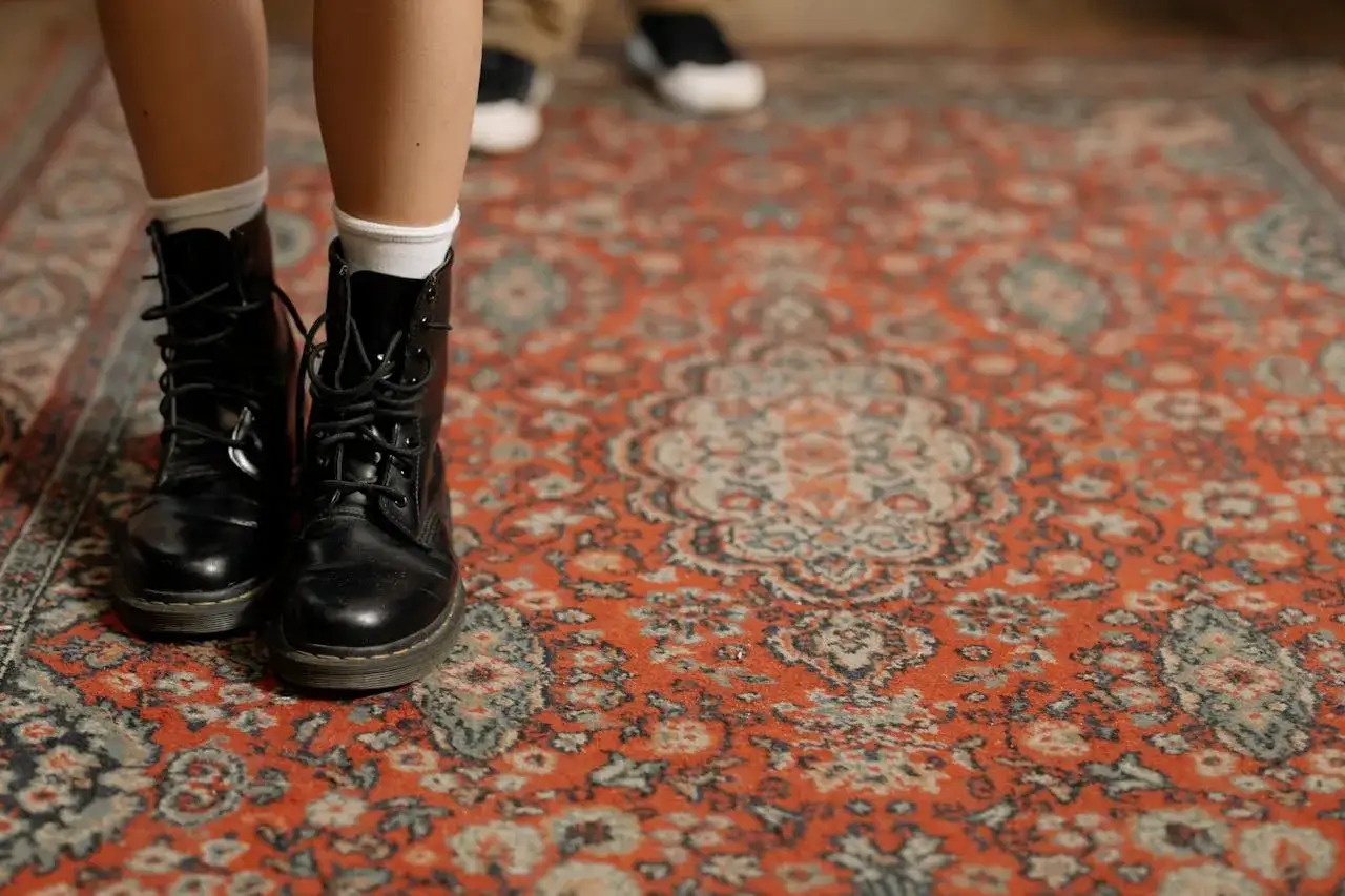 Schwarze Stiefel auf einem roten Perserteppich. Zeit, den schönen Teppich zu reinigen, damit er wieder strahlt.