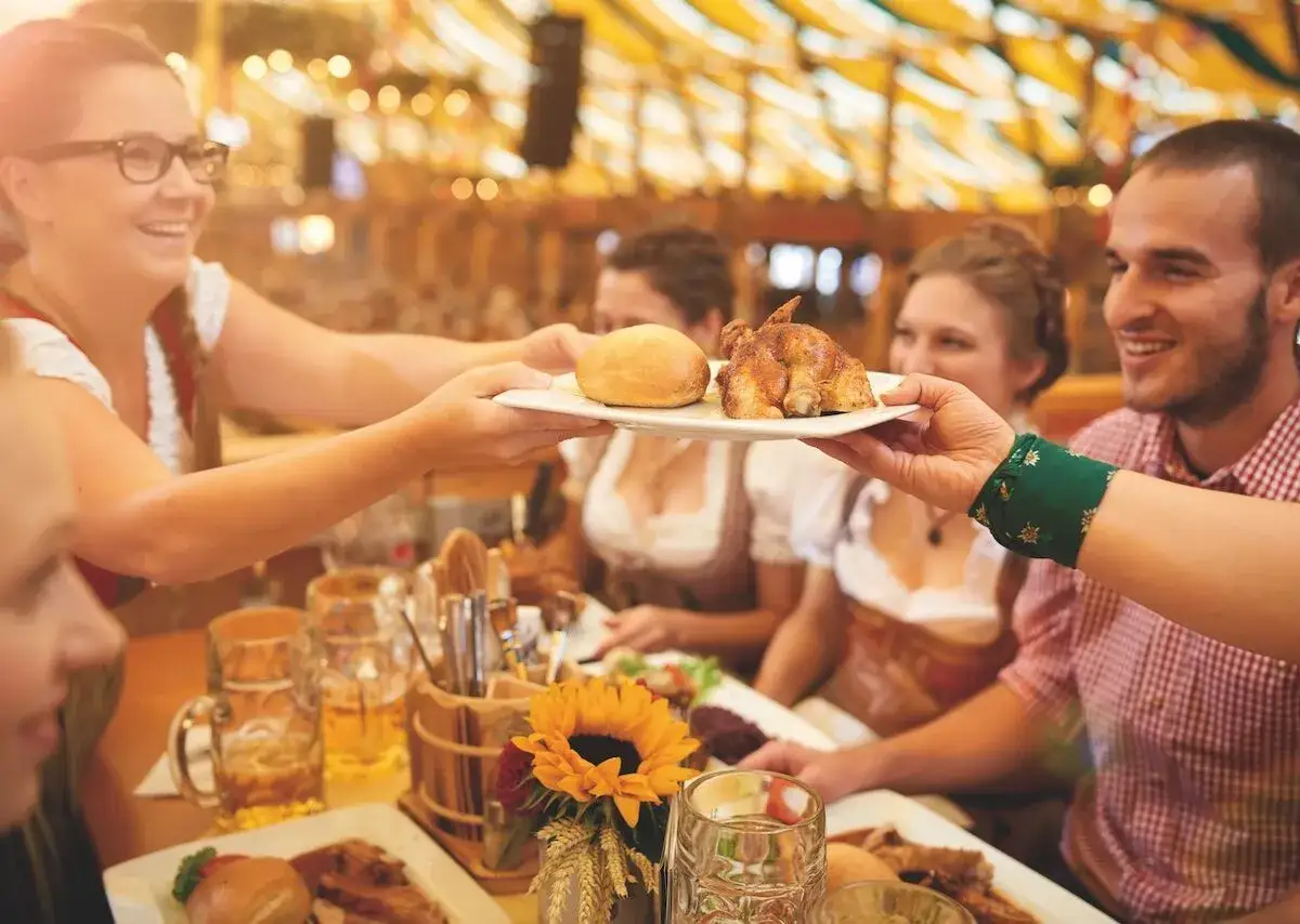 Freudige Menschen in Tracht genießen Hähnchen und Bier. Ein Fest für die Sinne, das Lust auf weitere interessante Reiseziele macht.