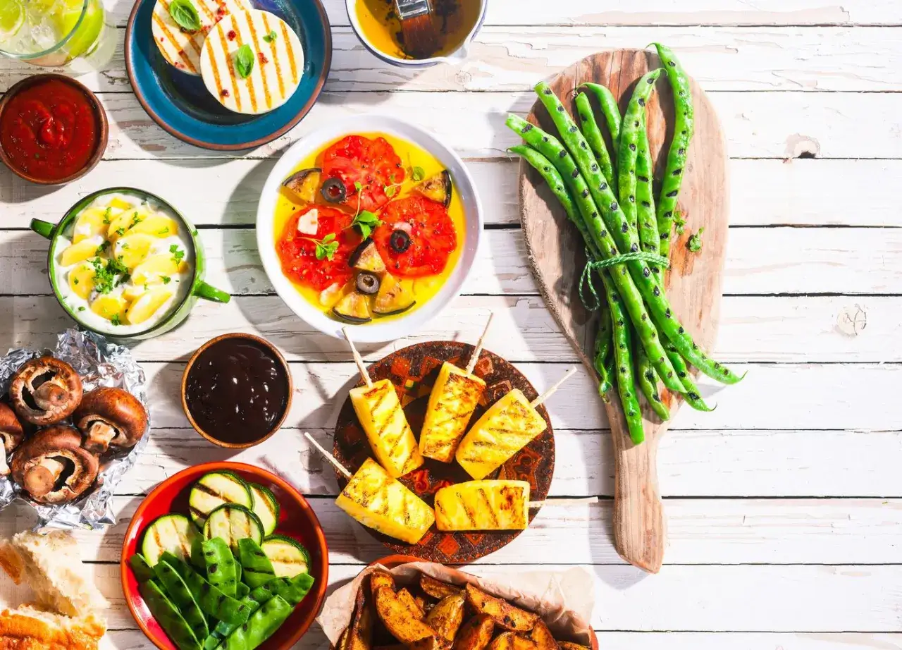Kolorowy stół z pysznym, zdrowym grillem: grillowany ser halloumi, szparagi, pomidory, cukinia, pieczarki i ananas.