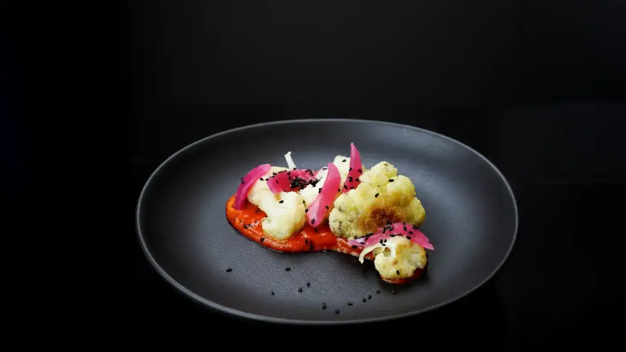 Coliflor asada con salsa roja, cebolla morada encurtida y semillas negras. Una deliciosa opción para tus recetas con coliflor.