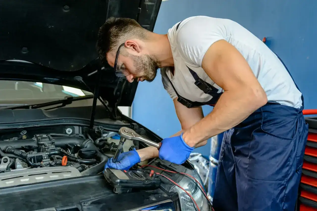 Mechanik w autoryzowanym serwisie samochodowym naprawia silnik, używając klucza nasadowego i miernika.