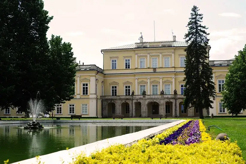 Piękny park w Puławach z pałacem w tle, fontanną i kolorowymi rabatami kwiatowymi.
