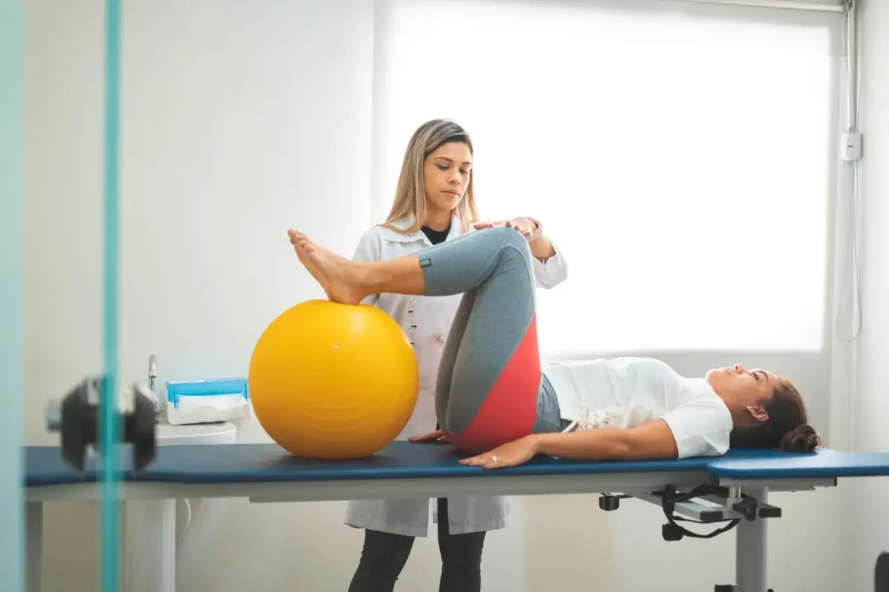 Fisioterapista assiste donna in esercizi per la diastasi addominale, usando una palla gialla.