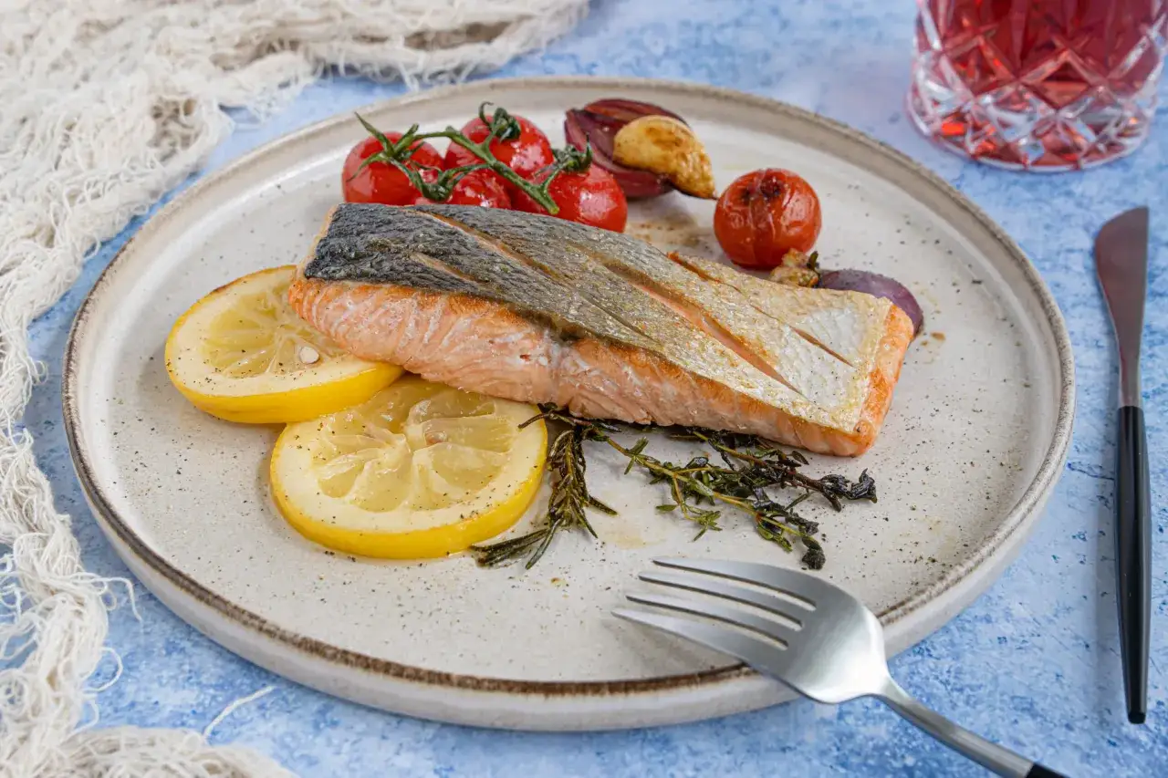 Perfekt gebratener Lachs mit Zitronenscheiben, Kirschtomaten und Kräutern auf einem Teller.