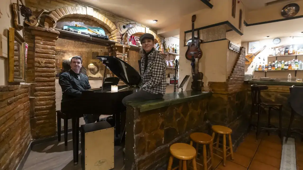 Pareja disfruta de música en vivo en un bar clandestino Zaragoza. Piano, guitarras y ambiente acogedor.