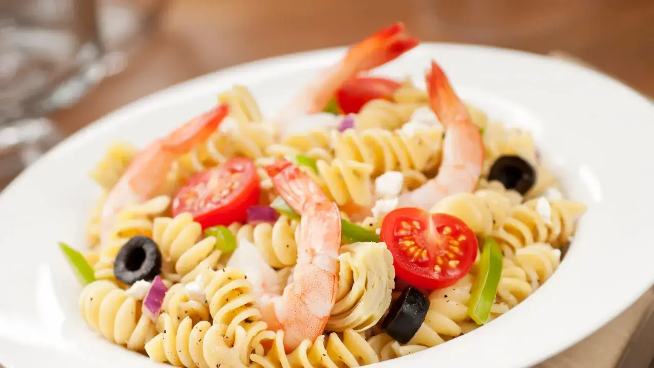 Un piatto invitante di pasta con gamberetti, pomodorini, olive nere e formaggio feta.