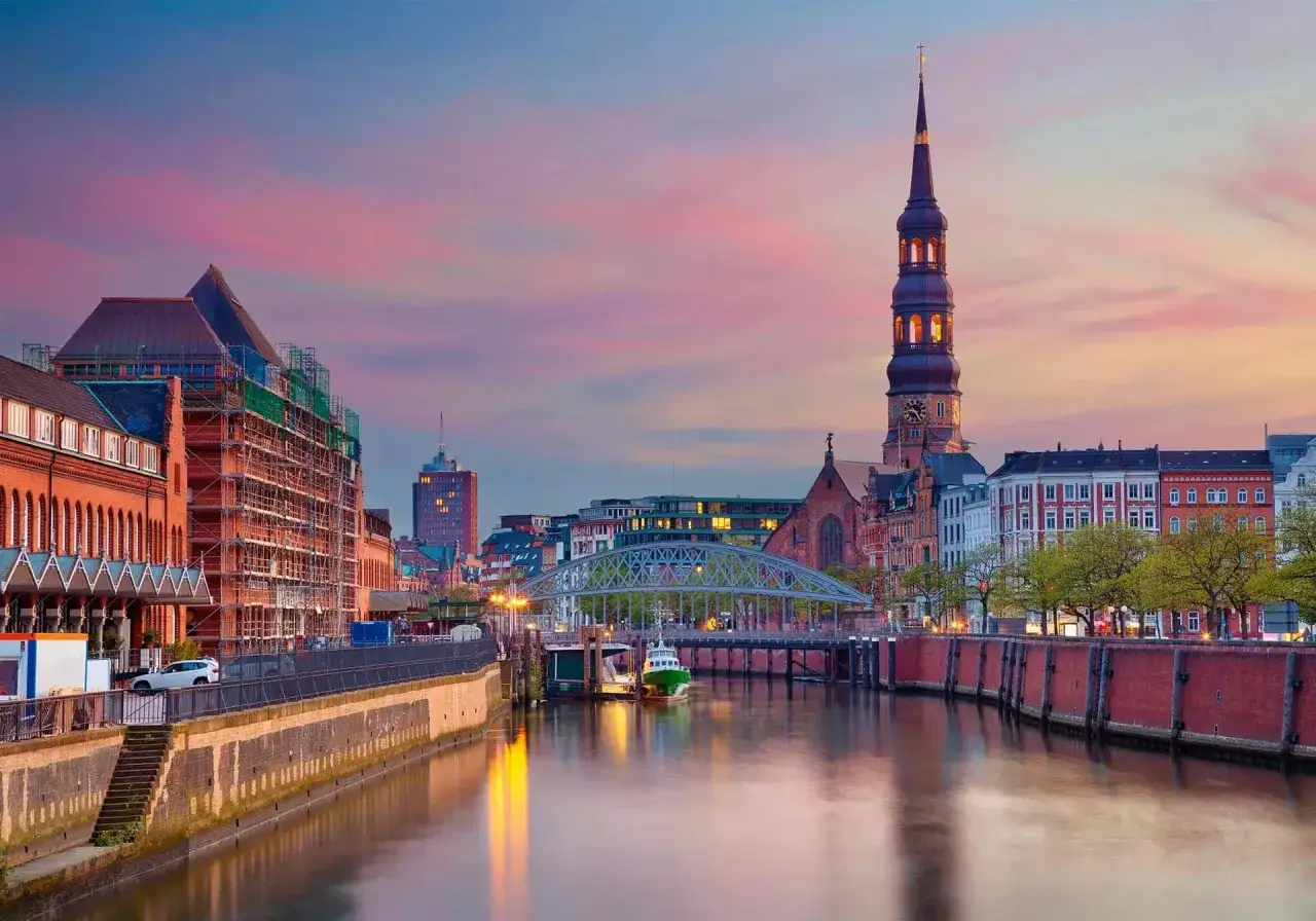 Hamburgs hamn vid solnedg&aring;ngen, en perfekt vy f&ouml;r din reseguide Hamburg. En gr&ouml;n b&aring;t ligger vid kajen under en bro.