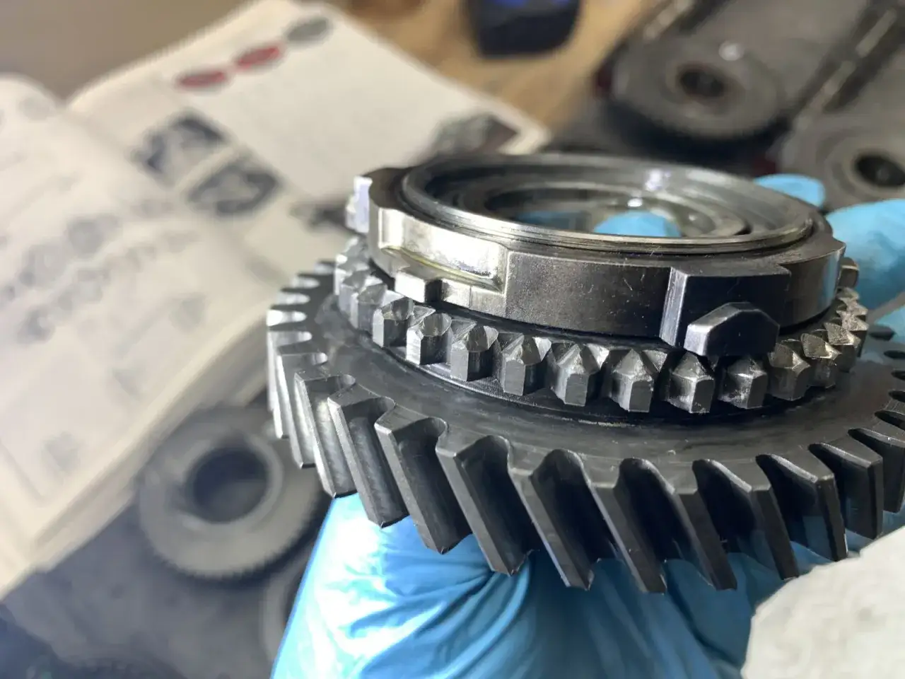 Metalowy synchronizator 2 biegu w dłoni, obok otwarta instrukcja serwisowa.