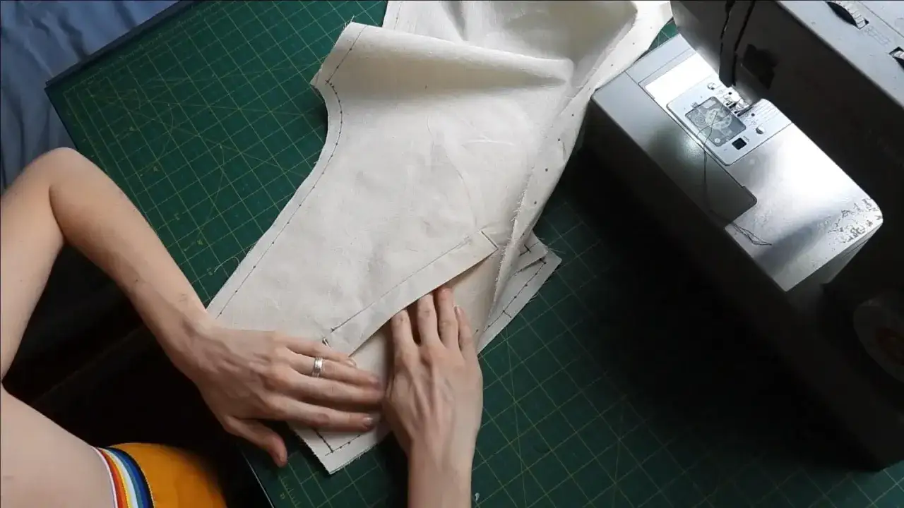 Mains travaillant sur un patron de couture, créant une poche raglan sur un tissu écru, à côté d'une machine à coudre Singer.