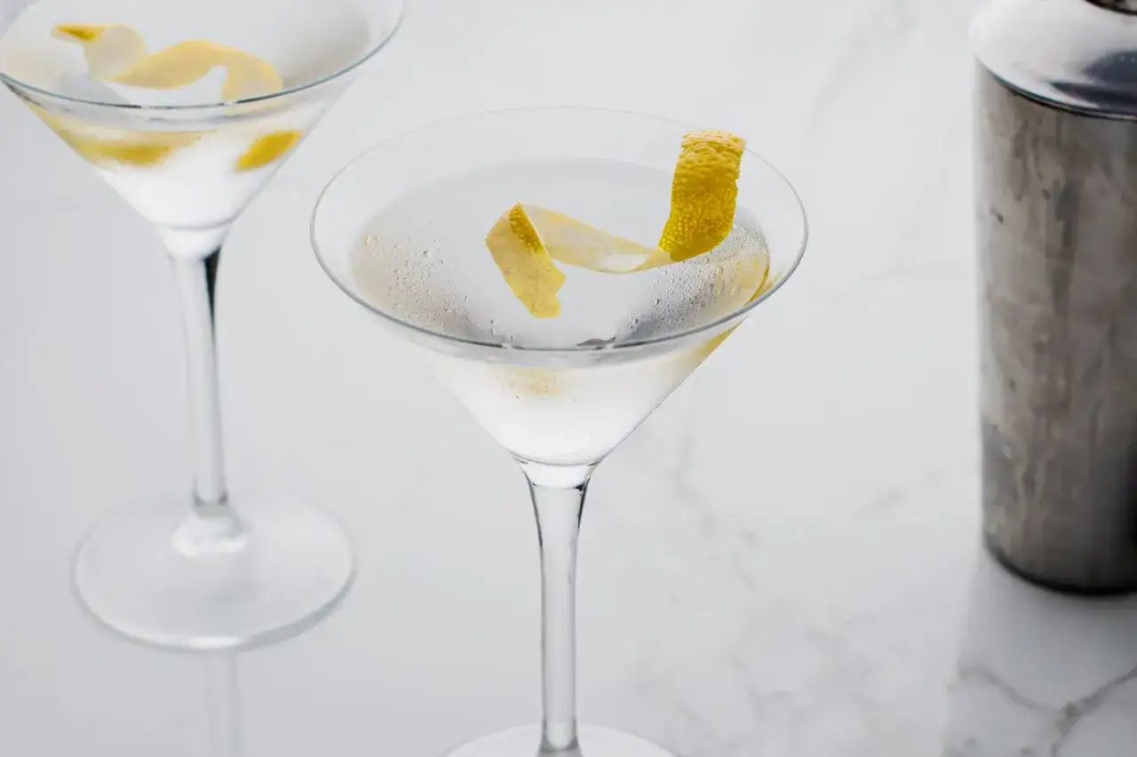 Dwa schłodzone martini, drink Jamesa Bonda, z cytrynową skórką i shakerem w tle.