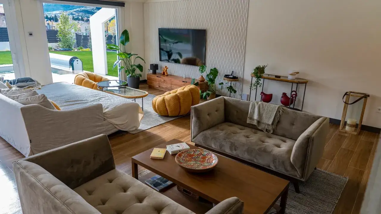 Sal&oacute;n moderno con sof&aacute;s grises, mesa de centro de madera y una llamativa pared prefabricada interior con textura detr&aacute;s del televisor.