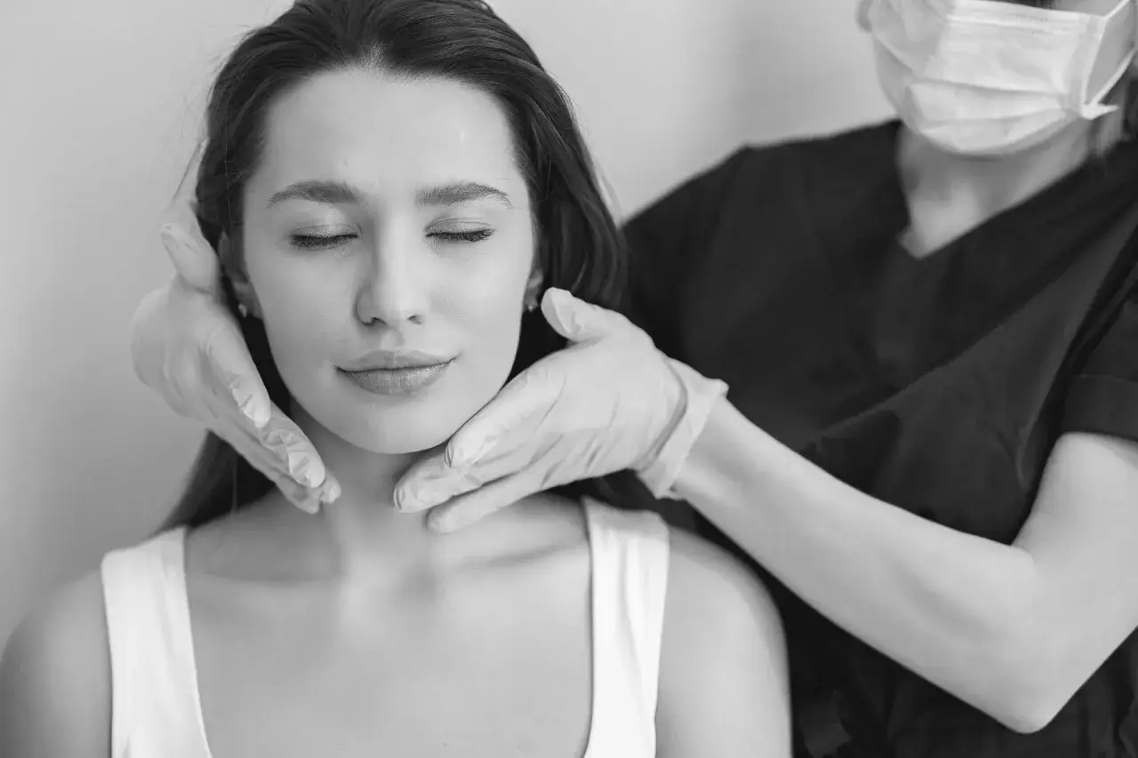 En kvinna med slutna ögon får sitt ansikte undersökt av en person i skyddsmask och handskar. Kanske förbereder hon sig för att ligga ner efter botox.