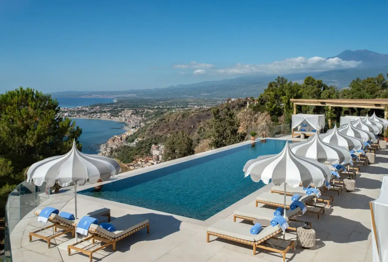 Oändlig pool med utsikt över Siciliens kust. Solstolar och parasoller redo för gäster på White Lotus Sicily.