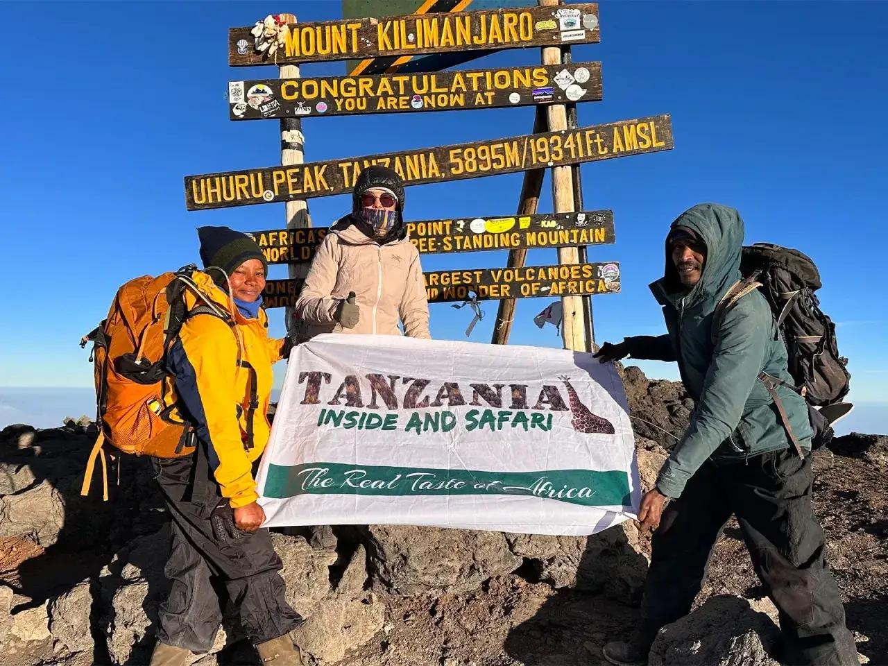 Trzy osoby świętują na szczycie Kilimandżaro. Czas wejścia na Uhuru Peak, 5895m.