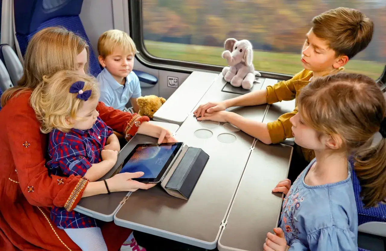 Rodzina w przedziale dla osoby z dzieckiem do lat 6 Intercity. Dzieci oglądają bajki na tablecie, podróżując pociągiem.