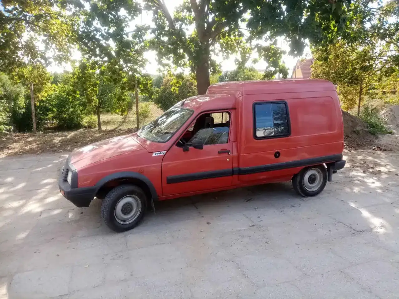 Czerwony Citroen C15, wierny towarzysz podróży, zaparkowany na tle zieleni i słońca.