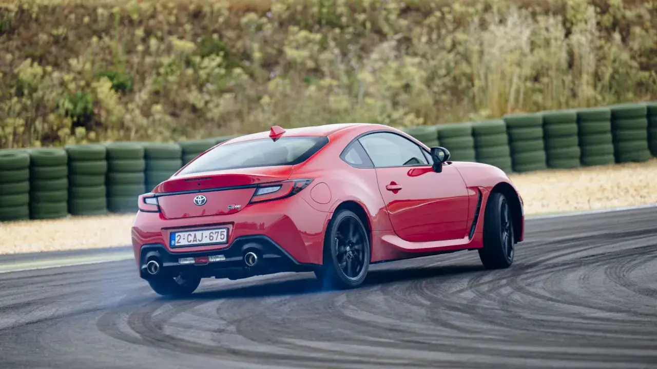 Toyota sportiva rossa in derapata su pista, con fumo dagli pneumatici e barriera di gomme verdi sullo sfondo.
