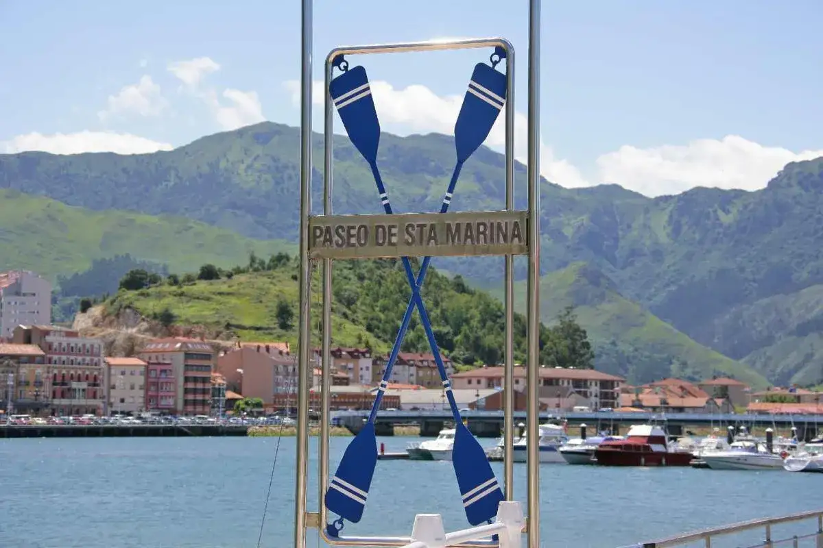 Paseo de Sta. Marina con remos cruzados, barcos en la bahía y montañas verdes al fondo.