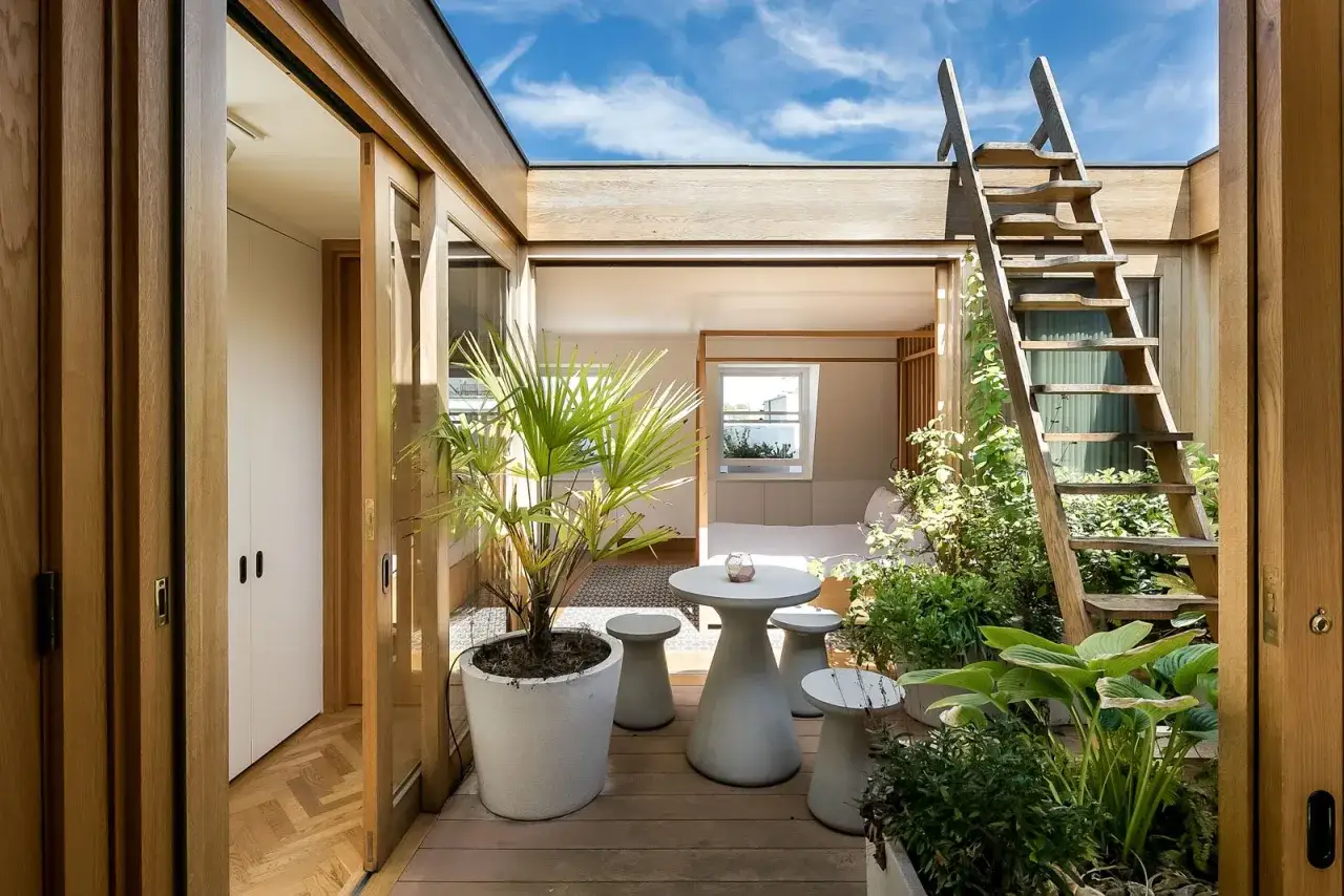 Terraza con plantas y muebles modernos, acceso a casas de dos plantas sencillas con terraza. Escalera de madera al cielo azul.