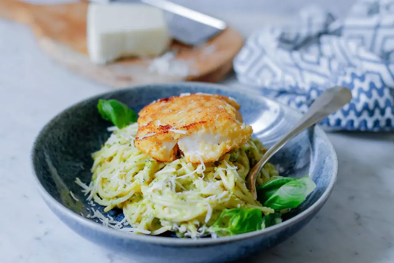 Pyszna ryba z makaronem w kremowym sosie, posypana parmezanem i udekorowana bazylią.