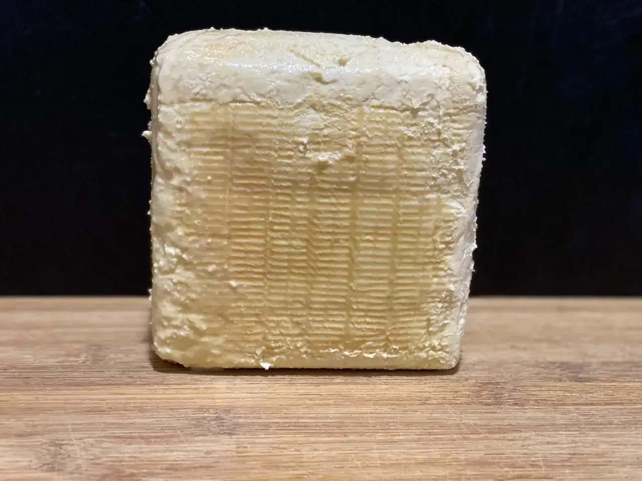 Un bloc de le vieux lille fromage, &agrave; la cro&ucirc;te textur&eacute;e et l&eacute;g&egrave;rement humide, repose sur une planche en bois.