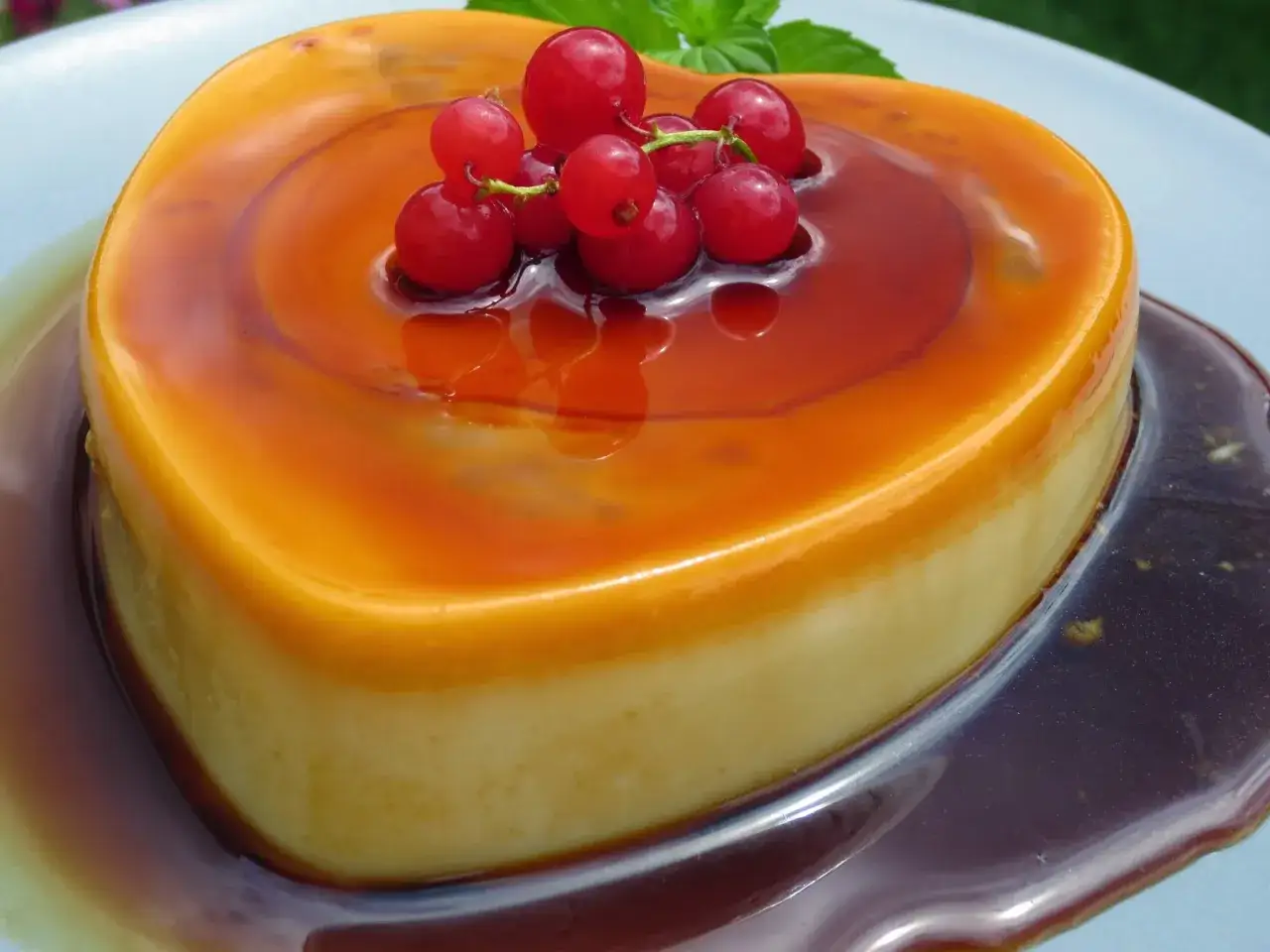 Corazón de flan de cuajada bañado en caramelo líquido, coronado con grosellas rojas y una hoja de menta.